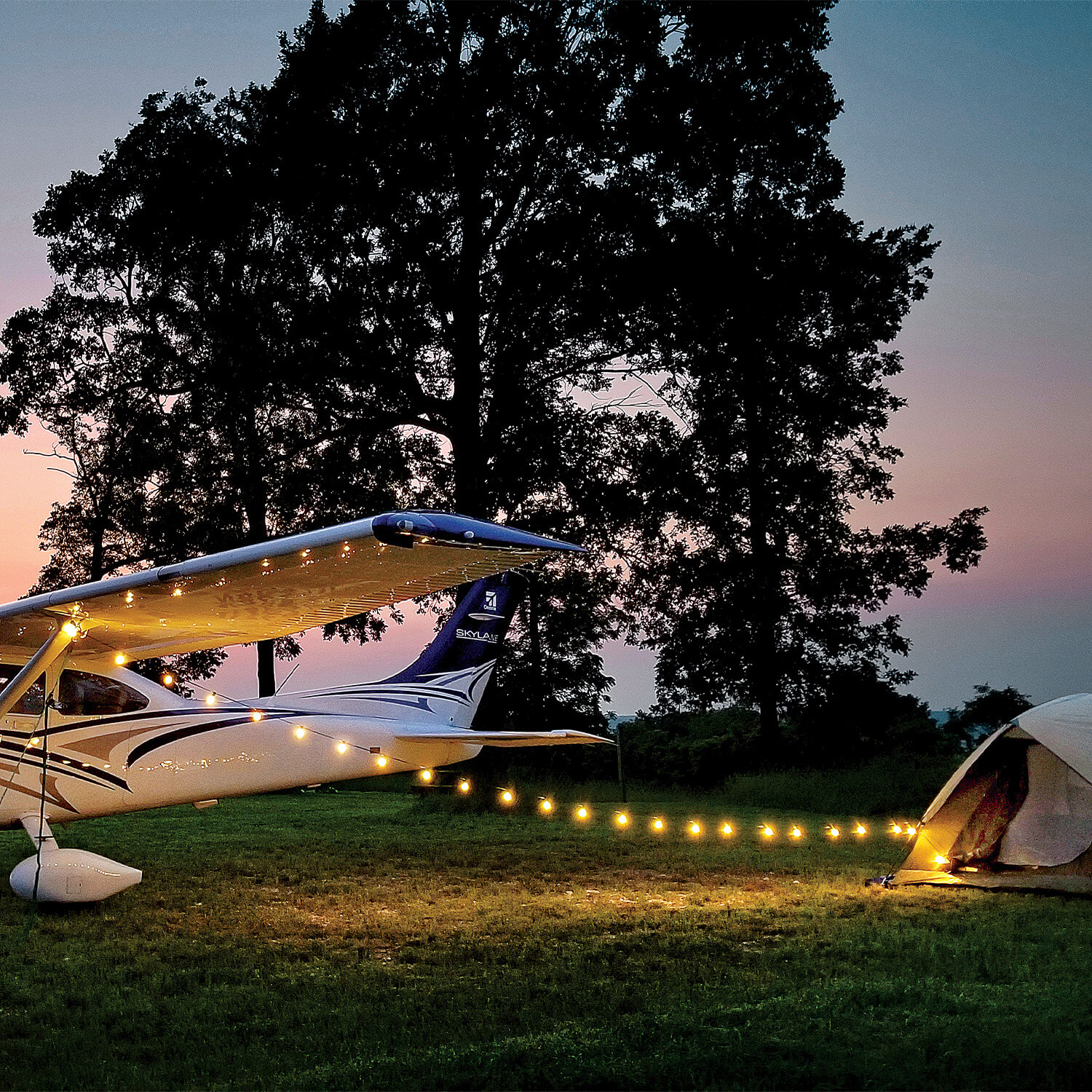 Cessna Skylane at a camp site next to a tent with lights.